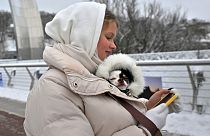 امرأة تتفحص هاتفها الذكي وهي تمسك بكلب في سترتها في كييف. 2023/11/22