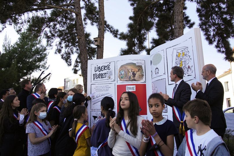 Children unveil a book sculpture as part of a tribute ceremony to French history and geography teacher Samuel Paty.