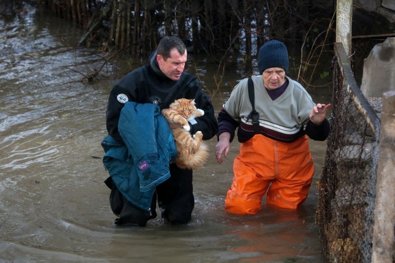 A rescuer carries a cat and helps a woman during an evacuation of residents of the flooded village of Pribrezhnoe in Crimea on November 27, 2023, following a storm.