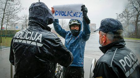 A Lubiana, un manifestante con in mano un cartello che recita: "ipocriti" affronta gli agenti di polizia durante la commemorazione delle vittime del COVID-19.