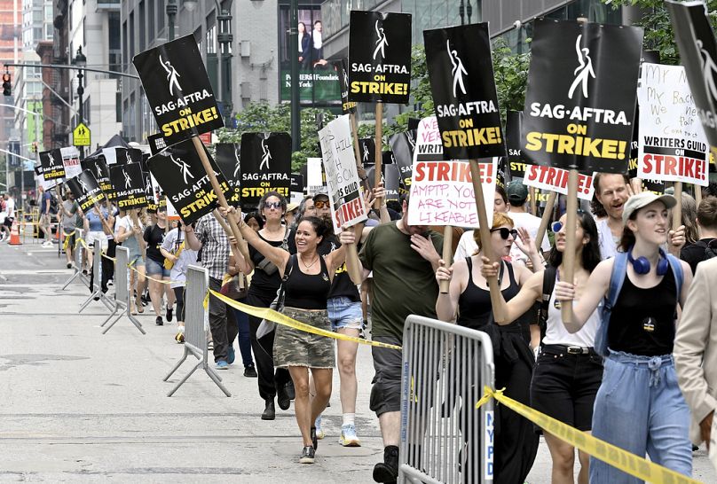 Protestocular, 18 Temmuz 2023 Salı günü New York'ta Amazon ve HBO stüdyolarının dışında pankartlar taşıyor.