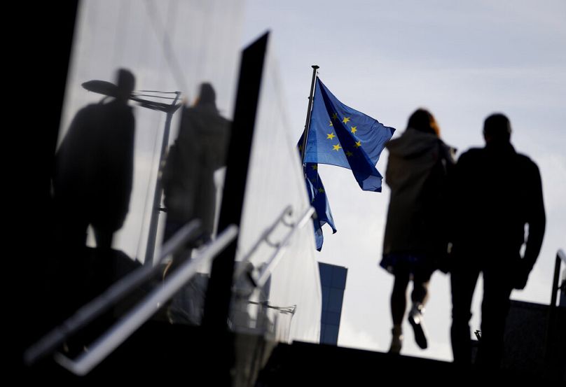 A couple walk past EU flags outside EU headquarters in Brussels, October 2021