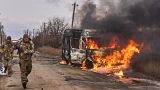 جنود أوكرانيون يمرون بالقرب من حافلة تحترق بعد أن ضربتها طائرة روسية بدون طيار بالقرب من باخموت