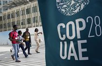 Az Egyesült Arab Emírségekben, Dubajban 2023. november 29-én, szerdán, az ENSZ COP28 klímacsúcs logója közelében sétáló emberek