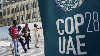 People walk near a logo for the COP28 U.N. Climate Summit, Wednesday, Nov. 29, 2023, in Dubai, United Arab Emirates.