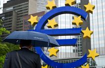 A man shelters from the rain under an umbrella as he walks past the Euro currency sign in front of the former European Central Bank (ECB) building in Frankfurt am Main, wester