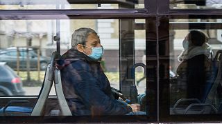 A man wearing a protective face mask sits in a city bus in Latvia.