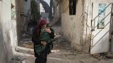 امرأة فلسطينية تحمل طفلًا وتهرب في أحد شوارع مخيم جنين بعد اجتياحه من قبل الجيش الإسرائيلي