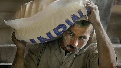 عامل فلسطيني يحمل كيساً من الدقيق بعد تفريغه من شاحنة في مركز توزيع تابع للأونروا
