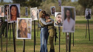 Varios israelíes se abrazan junto a las fotos de las personas asesinadas y secuestradas por militantes de Hamás durante su asalto al festival de música Nova, en el sur de Israel.
