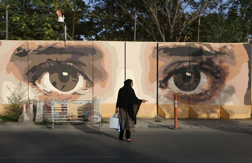 An Afghan woman waits for transportation in front street art on a barrier wall of the NDS (National Directorate of Security) in Kabul, August 2015