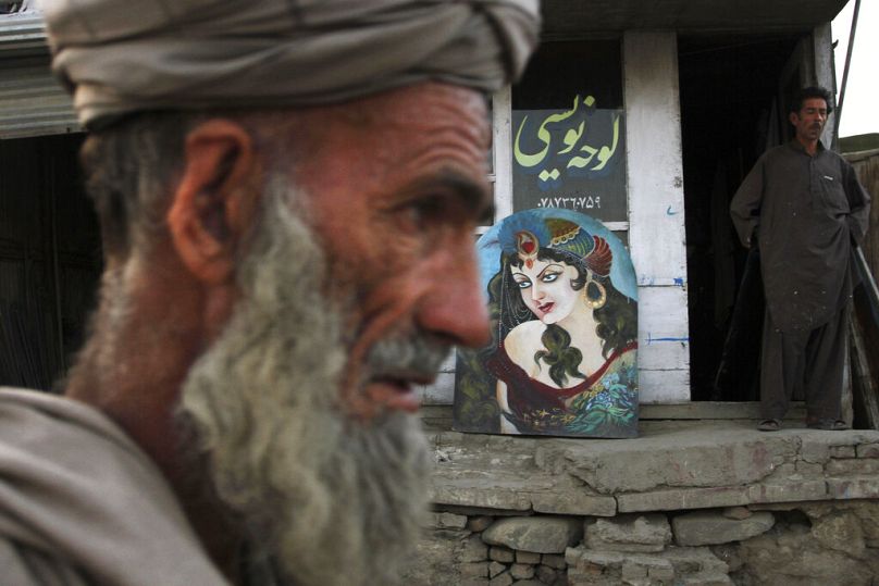 An elderly Afghan man walks past by a painted tableau depicting a woman outside Shaker's painting shop in Kabul, June 2011