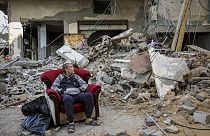 A Palestinian man sits in an armchair outside a destroyed building in Gaza City