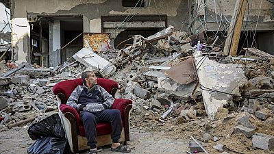 A Palestinian man sits in an armchair outside a destroyed building in Gaza City