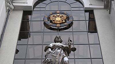 A statue of Themis, an ancient Greek Goddess of Justice, and a Russian national state emblem are seen at the entrance of Russia's Supreme Court in Moscow