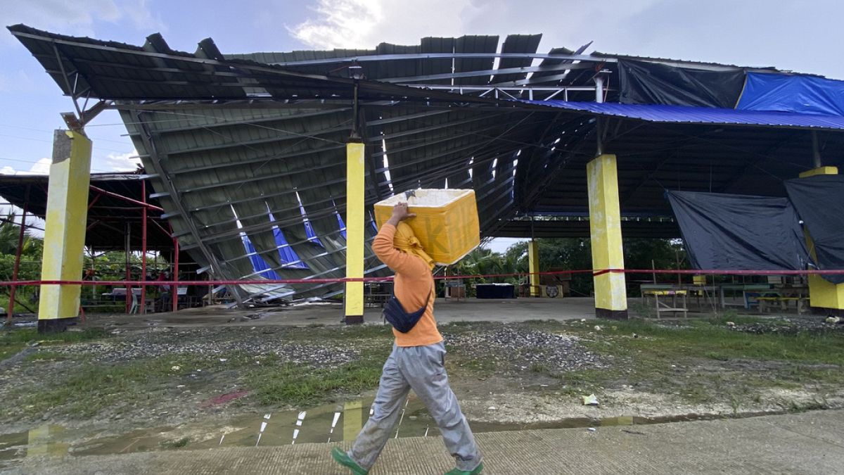 A fish vendor passes by a partially collapsed multipurpose covered court in Tagbina town, Agusan del Sur, southern Philippines on Sunday Dec. 3, 2023.