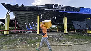 A fish vendor passes by a partially collapsed multipurpose covered court in Tagbina town, Agusan del Sur, southern Philippines on Sunday Dec. 3, 2023.