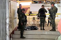 Military personnel stand guard at the entrance of a gymnasium while police investigators  look for evidence.