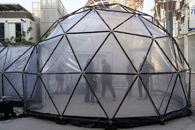 Persone in una capsula progettata per imitare la qualità dell'aria di Nuova Delhi durante il vertice sul clima delle Nazioni Unite a Dubai