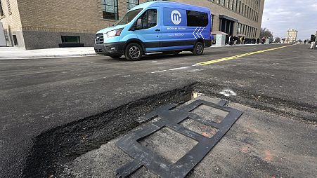 An electric van drives near a visible in-road wireless charging coil to be installed in a street in Detroit, Wednesday, November 29, 2023.