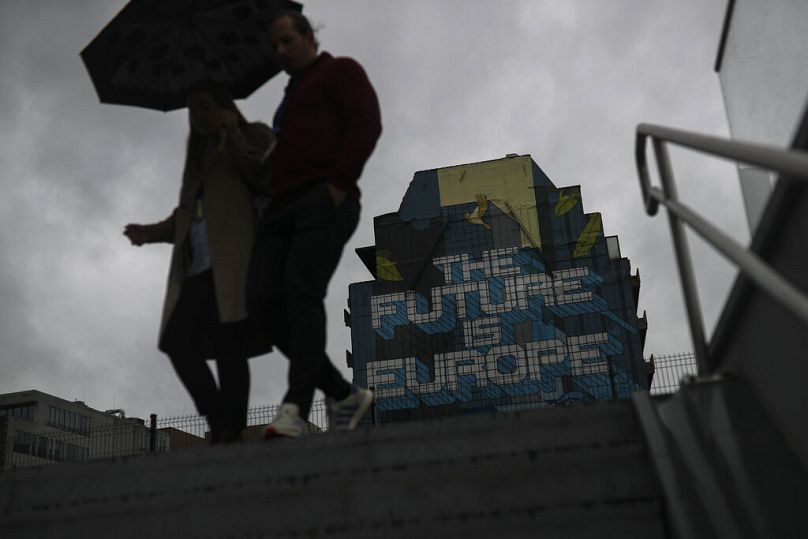 People shelter from the rain as they walk past street art near the European Commission headquarters in Brussels, September 2019