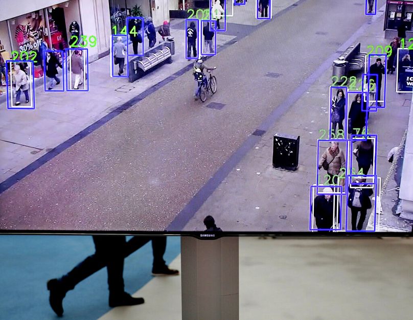 People walk behind a screen showing a prototype which can track people walking in a street during a technology fair at the European Parliament in Brussels, October 2019