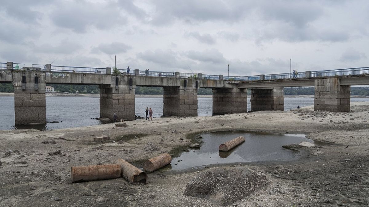 People walk on a central beach as a water in Dnipro river dropped for more than 4 meters after the explosion of the Kakhovka dam in Zaporizhzhia, Ukraine, Sunday, July 9, 2023