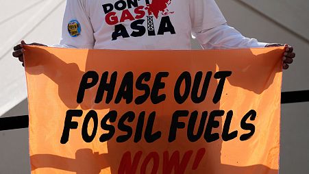 A person holds a sign reading "phase out fossil fuels now!" during a demonstration for a just and equitable transition from fossil fuels at COP28.