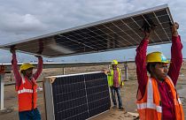 Workers carry a solar panel for installation at the under-construction Adani Green Energy Limited's Renewable Energy Park, India, 21 September 2023.