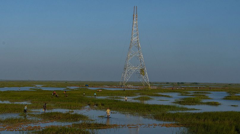Workers walk through a swamp to install electric transmission towers for the Adani Renewable Energy Park near Khavda,