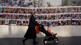 Женщина с ребенком в коляске на фоне стены с фотографиями заложников