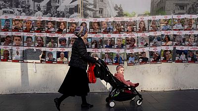 Eine Frau geht in Jerusalem mit ihrem Kinderwagen vor Bildern der Geiseln vorbei, 3. Dezember