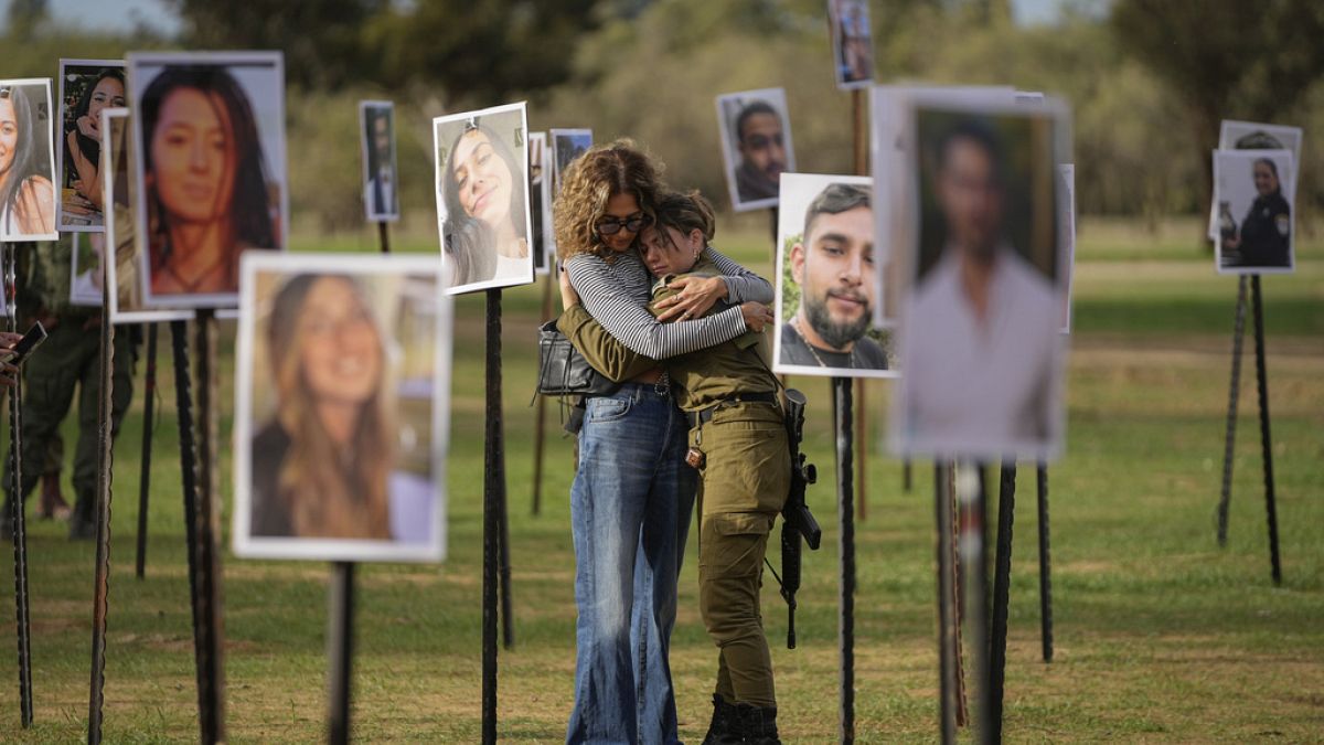 Israelis embrace next to photos of people killed and taken captive by Hamas militants during their violent rampage through the Nova music festival in southern Israel.