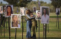 Israelis embrace next to photos of people killed and taken captive by Hamas militants during their violent rampage through the Nova music festival in southern Israel.