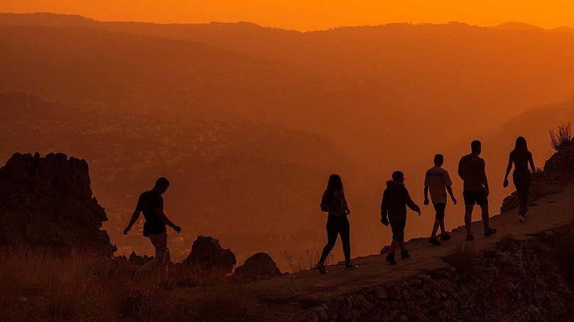 Des randonneurs marchent le long d'une falaise pour admirer le coucher de soleil sur la vallée de la Kadisha, un lieu saint pour les chrétiens maronites du Liban, le 21/07/23