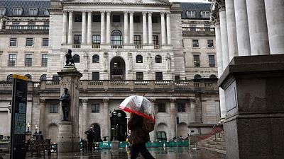 A pedestrian with an umbrella walks by the Bank of England building (rear C) and Stock Exchange building (R), in the financial district, central London, on November 2, 2023. H