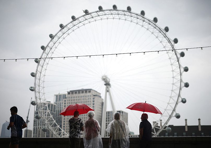 Pedestrians shelter from the rain beneath umbrellas while looking at the London landmark, the London Eye, from Embankment by the River Thames, in central London, on August 18,