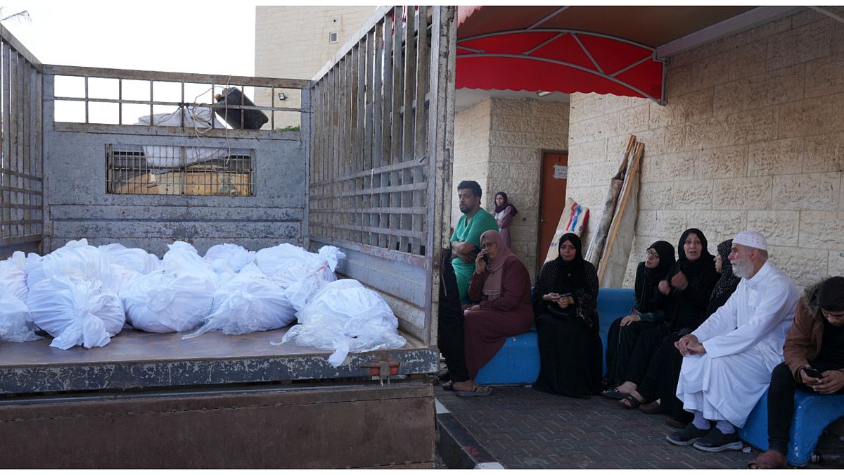 فلسطينيون يجلسون بالقرب من شاحنة مكدسة بالجثث أمام مستشفى الأقصى في غزة 