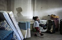 A girl walks amongst bags and mattresses as Eastern European migrants wait to temporarily settle in a locale in Decines, central-eastern France.