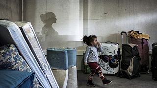 Una niña camina entre bolsas y colchones mientras migrantes de Europa del Este esperan para instalarse temporalmente en un local de Decines, en el centro-este de Francia.