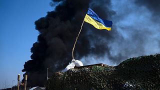 Un drapeau ukrainien au sommet d'un poste de contrôle alors que de la fumée noire s'élève d'un entrepôt de carburant ukrainien à la suite d'une attaque russe, près de Kiyv