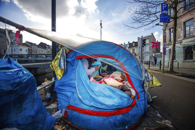 Two men share a meal in a makeshift tent camp outside the Petit Chateau reception center in Brussels, January 2023