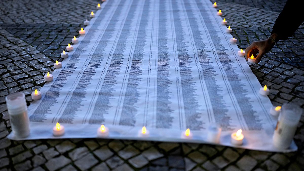لائحة بأسماء ضحايا القصف الإسرائيلي على غزة وبجانبها شموع مضاءة خلال وقفة اححتجاجية في لشبونة