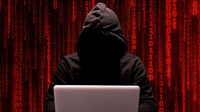A man in a hoodie typing on a computer.