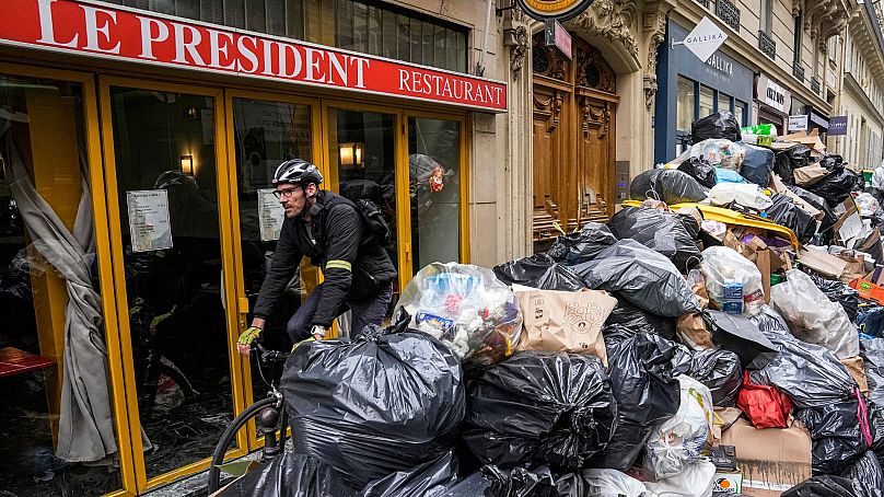 A cyclist rides past an uncollected rubbish pile next to a cafe in Paris, 21 March 2023.