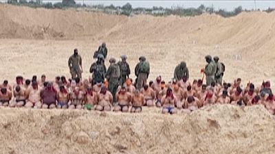 Palestinianos detidos em roupa interior são vigiados por soldados israelitas.