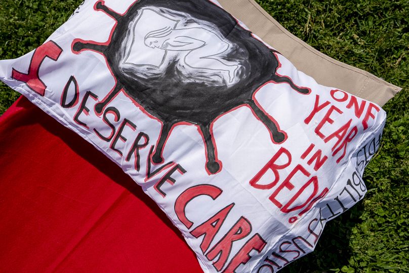 A pillow is decorated with the words "I Deserve Care" and "One Year in Bed!" as advocates for people suffering from long COVID-19 host an installation.