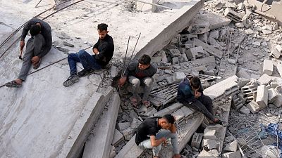 فلسطينيون يجلسون بالقرب من مبنى عائلة النادي الذي دمره القصف الإسرائيلي على قطاع غزة