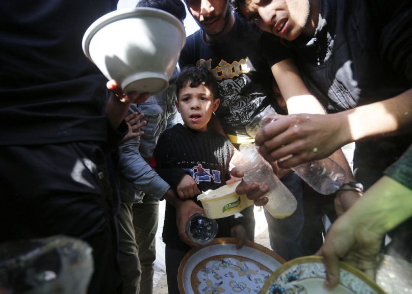 Displaced Palestinians, living in a tent camp in the city of Deir Al Balah, struggling with limited resources and difficult conditions, wait to receive soup from volunteers