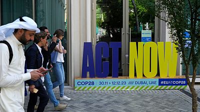 A group walks near a sign that reads "act now" at the COP28.